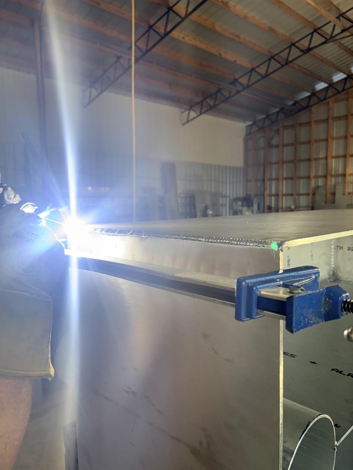 TIG welding the seam of a large aluminum box clamped on the bench in the Cobb's shop