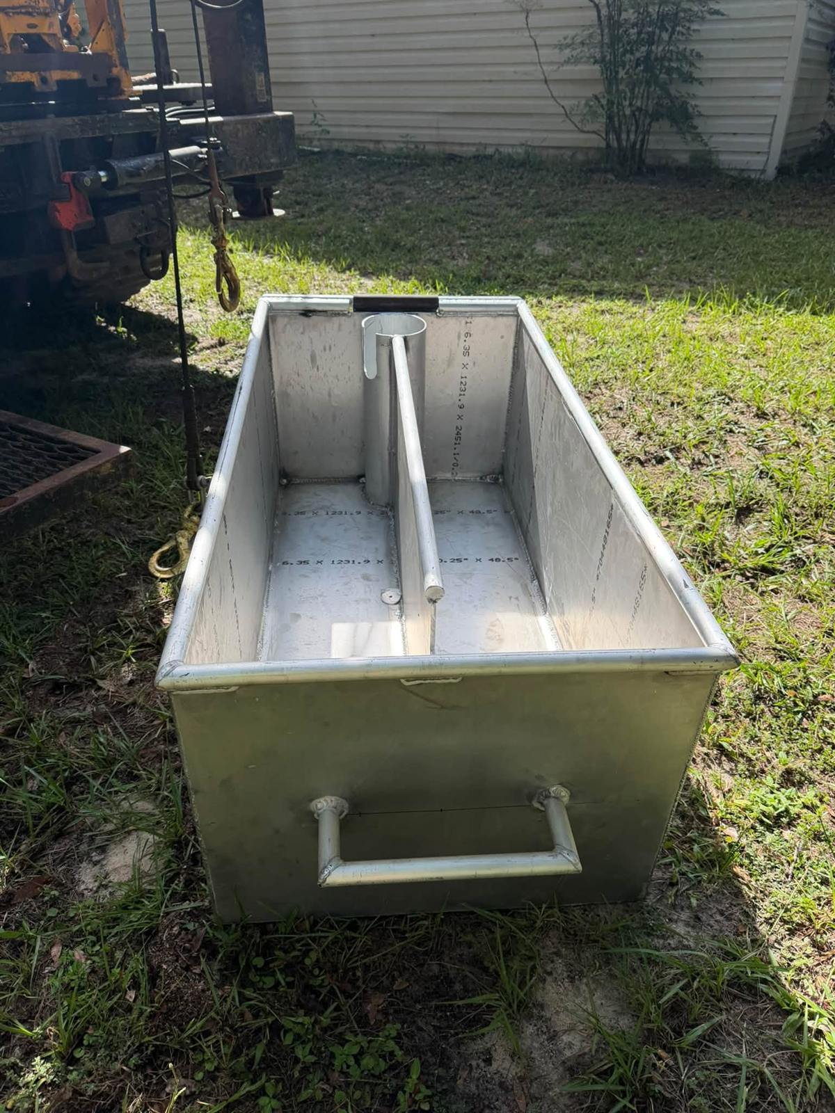 Welded aluminum trough with a center divider and side handle, sitting on grass