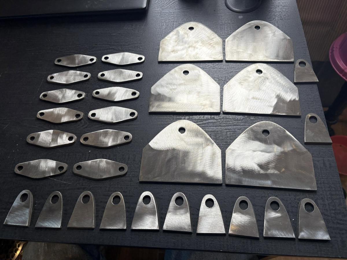 Rows of CNC plasma-cut steel tabs and gusset plates arranged on a dark table