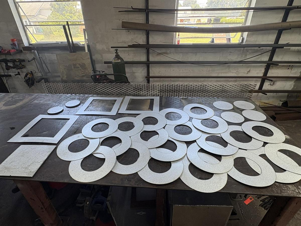 Dozens of CNC plasma-cut steel rings and plates laid out on the cutting table in the Cobb's shop