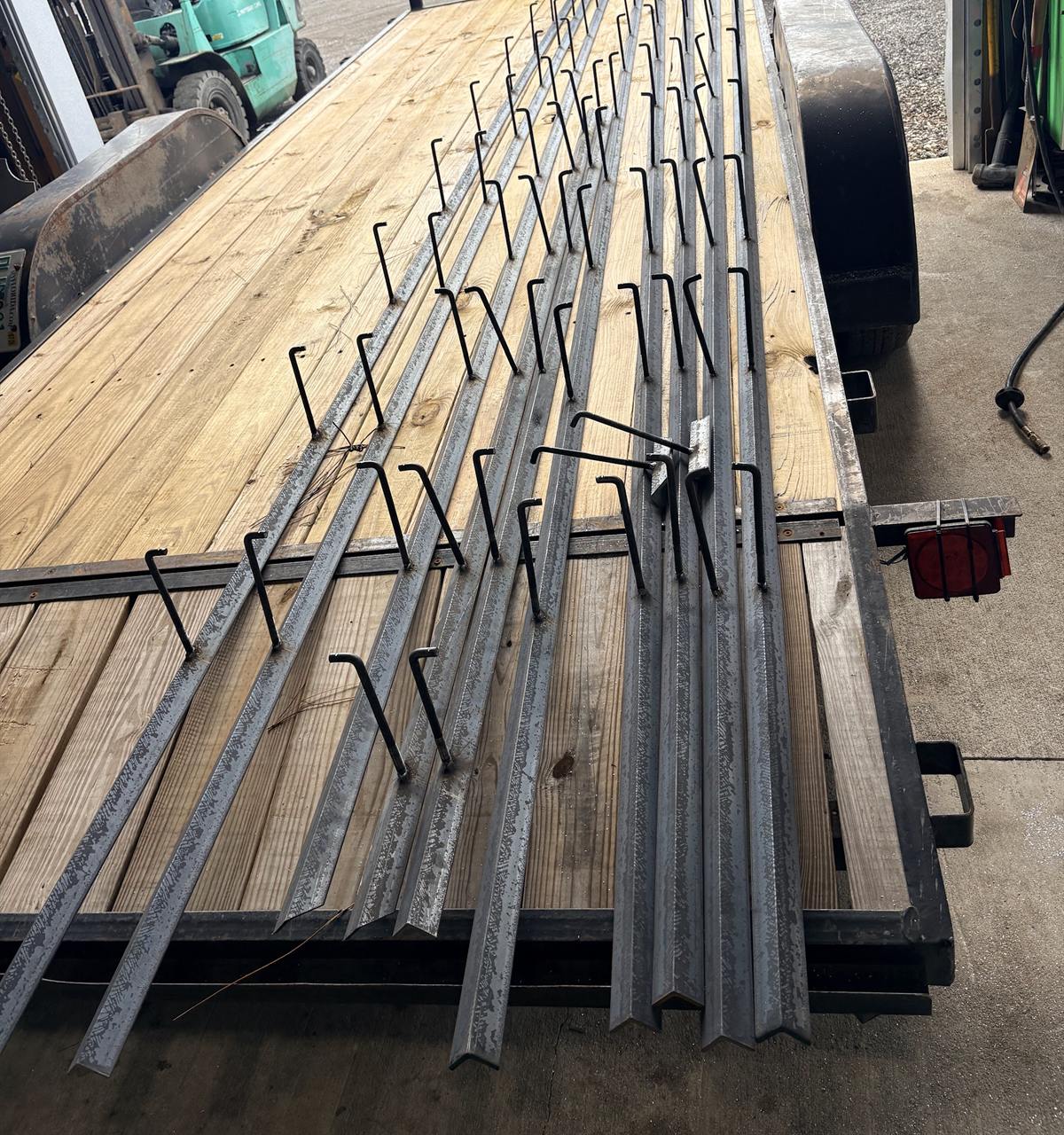 A long run of fabricated steel angle drain tracks with welded hooks, loaded on a flatbed trailer