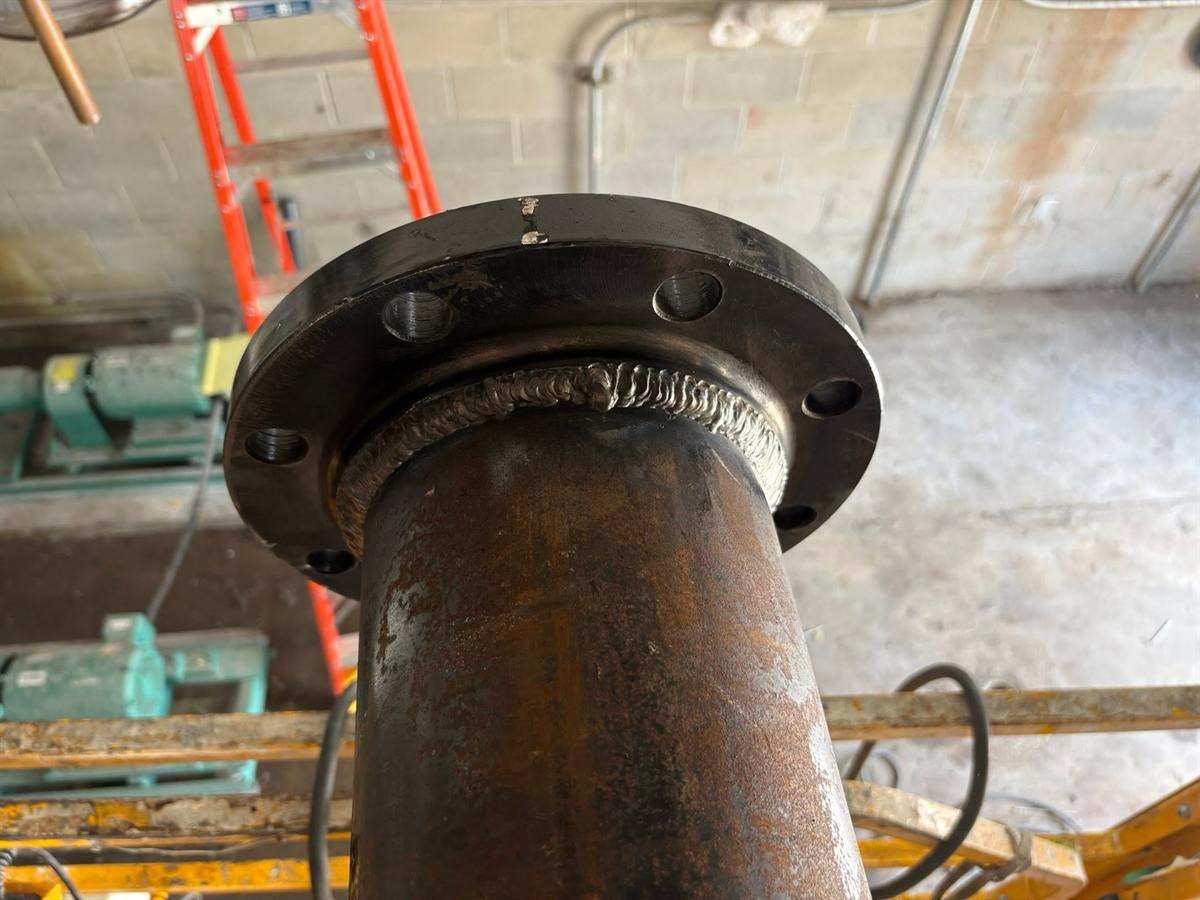 Close-up of a finished weld joining a steel pipe to a bolted flange